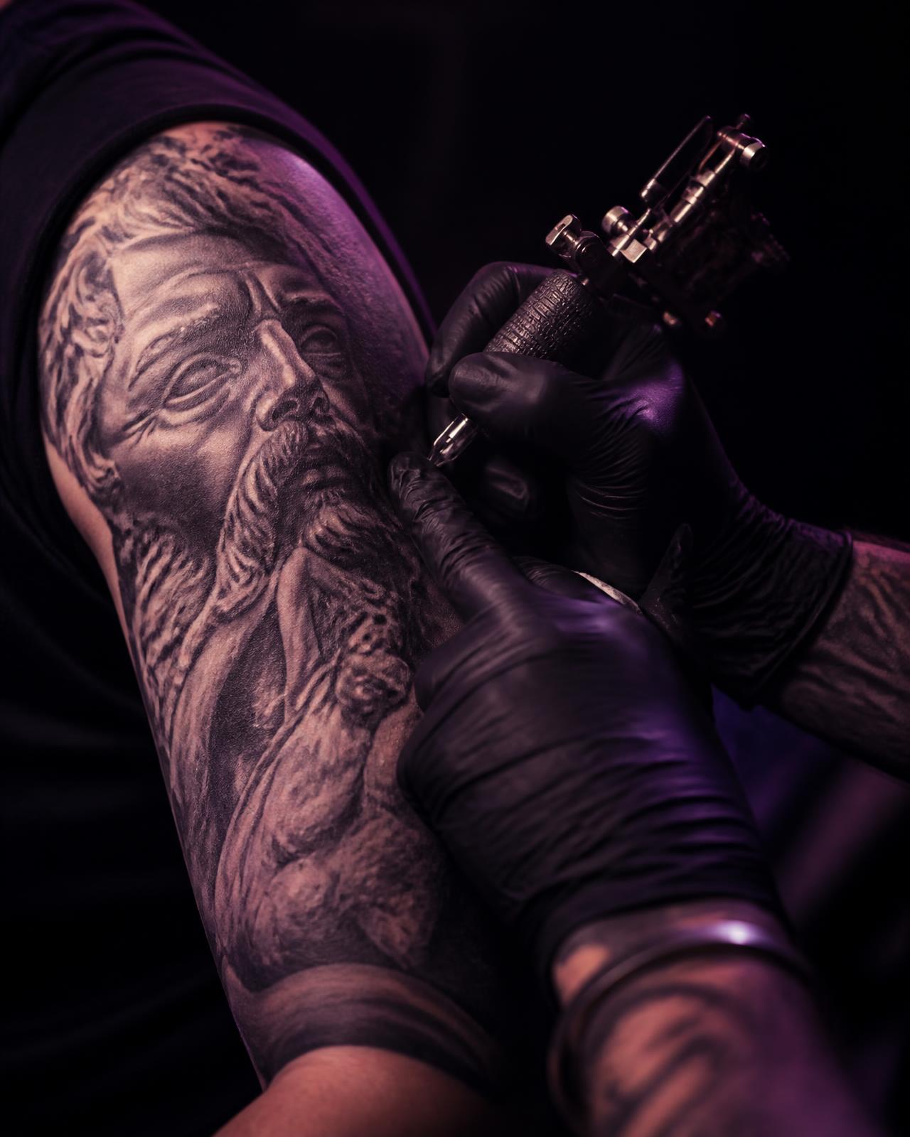 Tattoo artist working on a black and gray upper-arm piece
